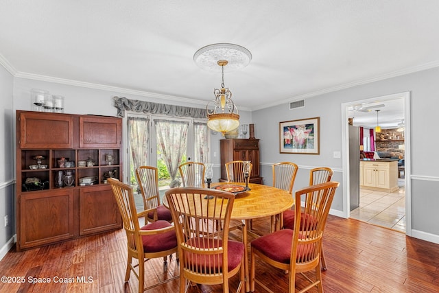 dining space featuring baseboards, visible vents, crown molding, and light wood finished floors