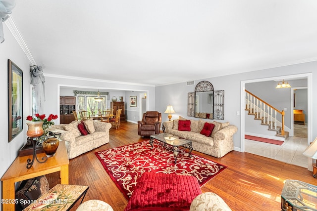 living area with crown molding, a notable chandelier, visible vents, wood finished floors, and stairs