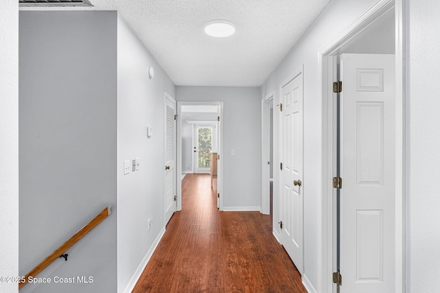 corridor with a textured ceiling, wood finished floors, and baseboards