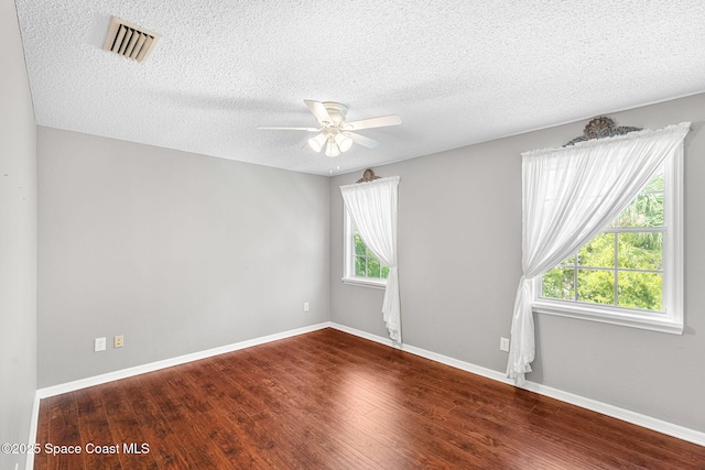 empty room featuring a textured ceiling, wood finished floors, a ceiling fan, visible vents, and baseboards