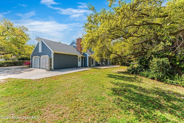 view of side of property featuring a yard, roof with shingles, a chimney, and driveway