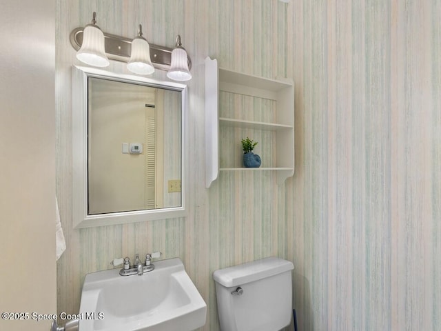 bathroom featuring toilet, wallpapered walls, and a sink