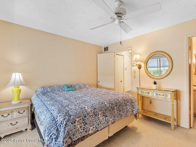 bedroom featuring visible vents, ensuite bathroom, a ceiling fan, light carpet, and a textured ceiling