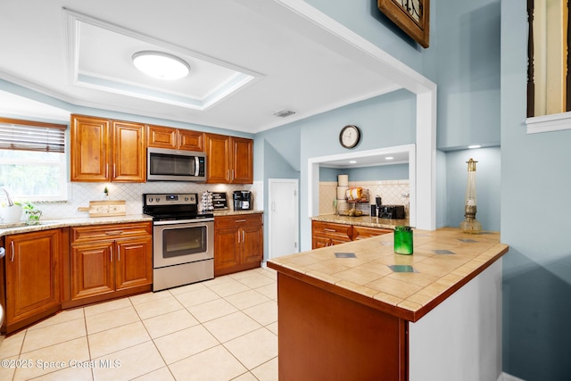 kitchen featuring stainless steel appliances, tasteful backsplash, brown cabinetry, and light tile patterned flooring