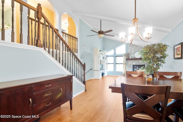 dining area with stairs, arched walkways, a fireplace, light wood-style flooring, and ceiling fan with notable chandelier