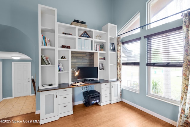 office area featuring light wood-type flooring, arched walkways, and baseboards