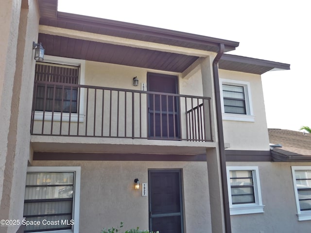 exterior space with a shingled roof, a balcony, and stucco siding