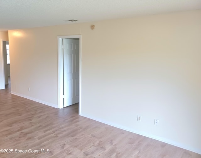 unfurnished room with visible vents, light wood-style flooring, baseboards, and a textured ceiling