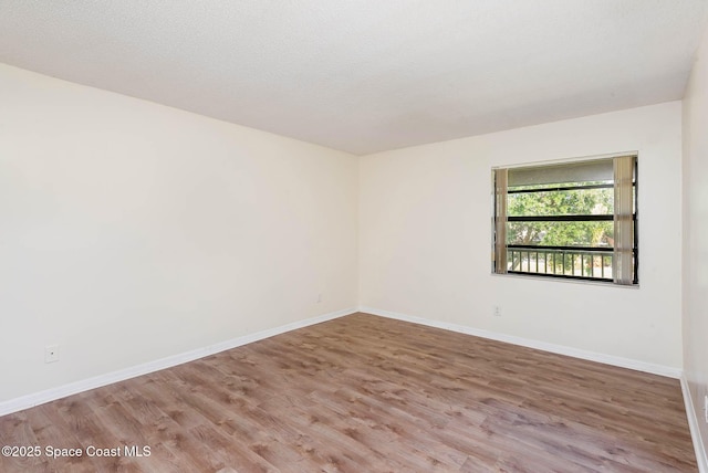 empty room featuring a textured ceiling, wood finished floors, and baseboards