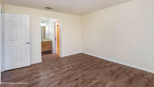 unfurnished bedroom featuring baseboards, visible vents, dark wood finished floors, ensuite bathroom, and a textured ceiling