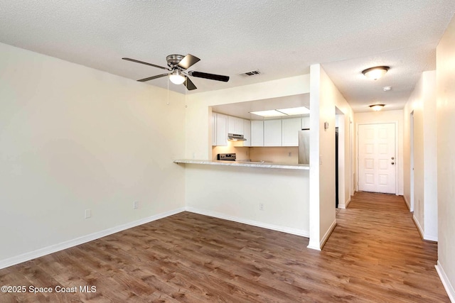 kitchen featuring stainless steel fridge, visible vents, wood finished floors, light countertops, and under cabinet range hood