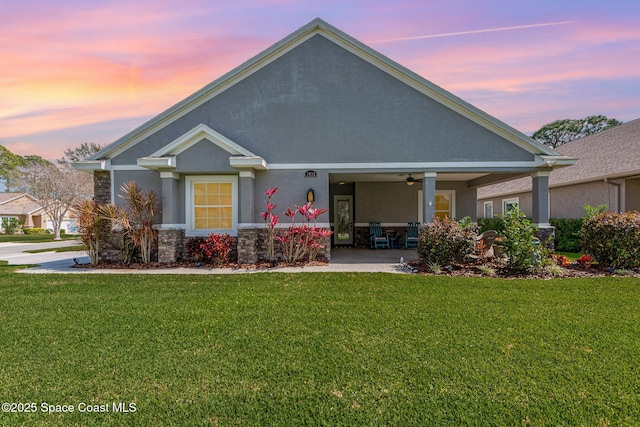 view of front of home featuring a ceiling fan, stone siding, a lawn, and stucco siding