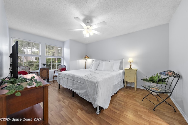 bedroom with light wood finished floors, ceiling fan, baseboards, and a textured ceiling