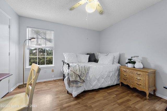 bedroom featuring a ceiling fan, a textured ceiling, baseboards, and wood finished floors