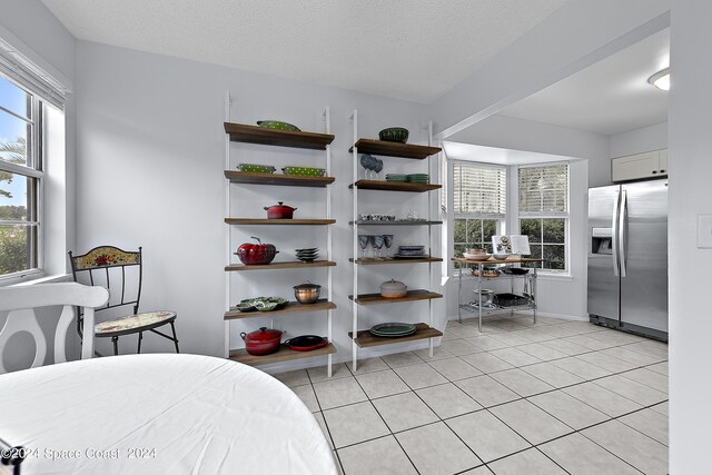 bedroom featuring a textured ceiling, multiple windows, light tile patterned flooring, and stainless steel fridge