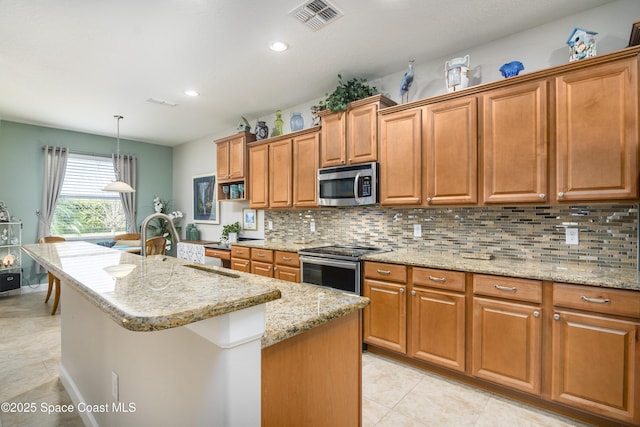 kitchen featuring brown cabinets, a center island with sink, stainless steel appliances, tasteful backsplash, and visible vents