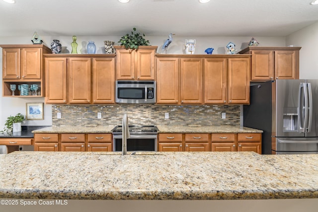 kitchen featuring a sink, appliances with stainless steel finishes, backsplash, and light stone counters