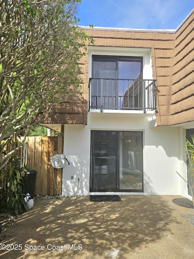 exterior space featuring mansard roof, a balcony, a tile roof, fence, and stucco siding