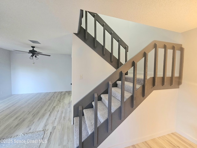 stairs featuring a textured ceiling, wood finished floors, visible vents, and a ceiling fan