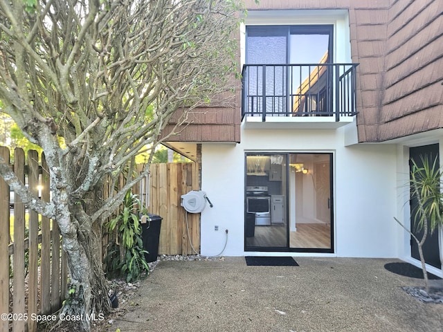 property entrance featuring a patio area, fence, a balcony, and stucco siding