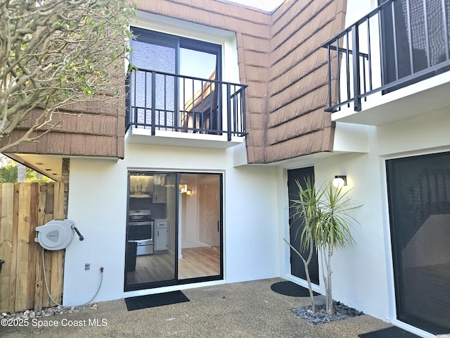 entrance to property with fence, a balcony, and stucco siding