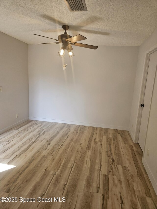 empty room featuring light wood-type flooring, visible vents, a textured ceiling, and baseboards