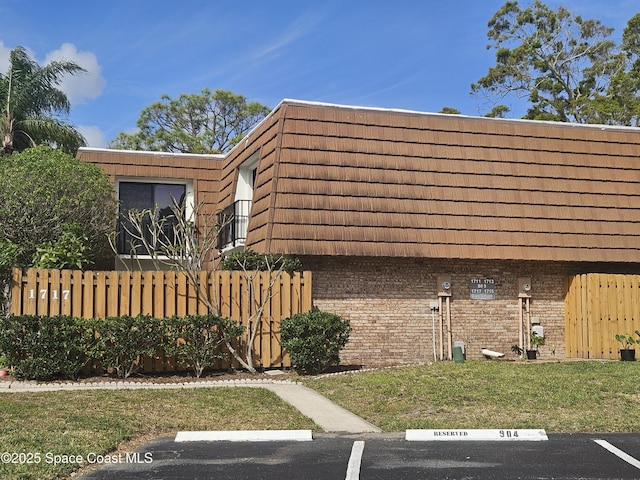 view of property exterior featuring mansard roof, a tile roof, fence, uncovered parking, and brick siding