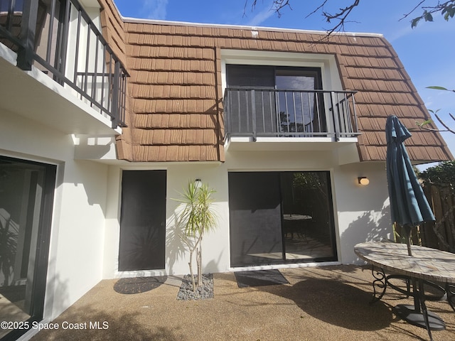 exterior space with mansard roof, a patio area, a balcony, and stucco siding