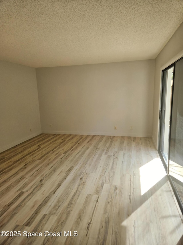 unfurnished room with a textured ceiling, light wood-type flooring, and baseboards