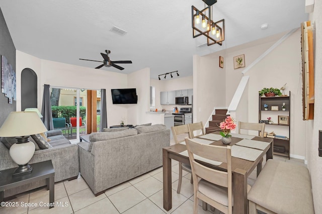 dining space featuring visible vents, stairway, rail lighting, ceiling fan with notable chandelier, and light tile patterned flooring