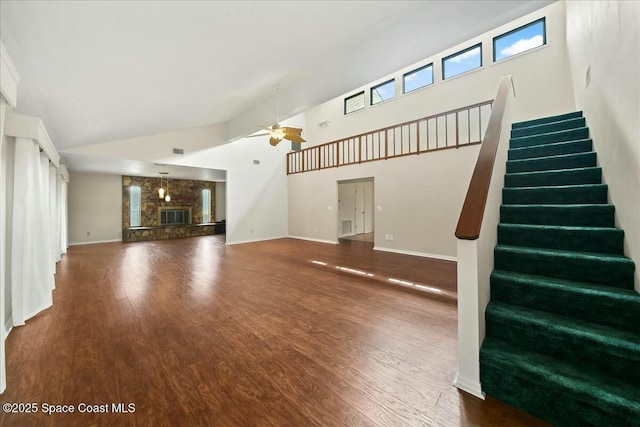 unfurnished living room with a ceiling fan, a stone fireplace, wood finished floors, high vaulted ceiling, and stairs