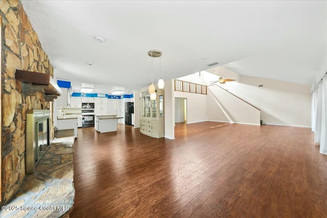 living area with ceiling fan, a stone fireplace, dark wood finished floors, and visible vents