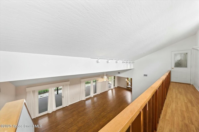 hallway with vaulted ceiling, a textured ceiling, track lighting, and wood finished floors