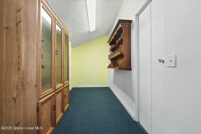 hallway with baseboards, dark colored carpet, and a textured ceiling