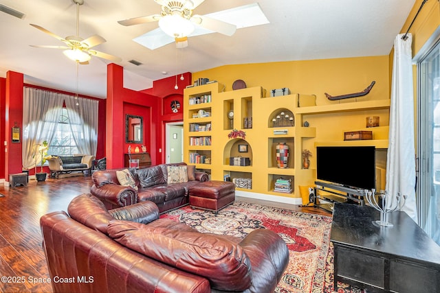 living area featuring a ceiling fan, vaulted ceiling with skylight, visible vents, and wood finished floors