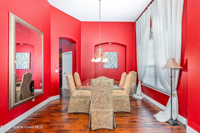 dining area with a chandelier, arched walkways, wood finished floors, and baseboards