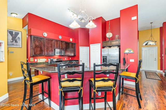 kitchen with stainless steel appliances, dark wood finished floors, baseboards, a kitchen bar, and decorative light fixtures