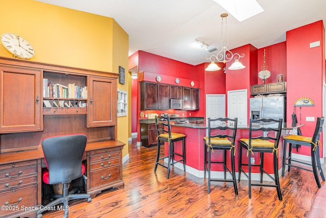 kitchen with a skylight, a breakfast bar area, dark countertops, appliances with stainless steel finishes, and wood finished floors