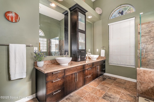 bathroom featuring a shower with door, a sink, baseboards, and double vanity