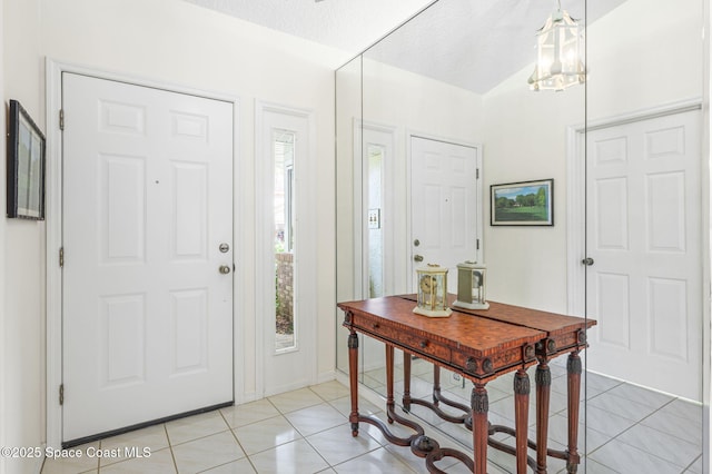 foyer with light tile patterned floors, a notable chandelier, vaulted ceiling, and a textured ceiling