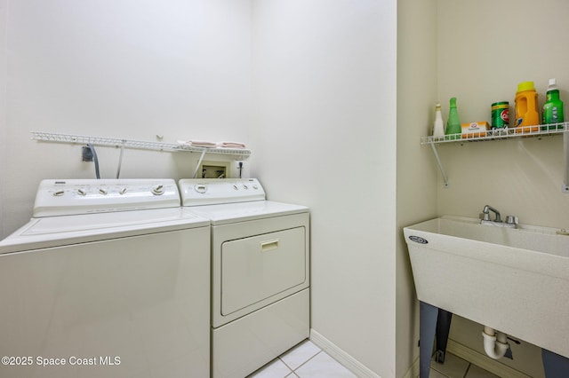 clothes washing area with light tile patterned floors, a sink, separate washer and dryer, laundry area, and baseboards