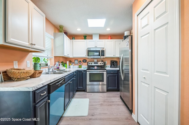 kitchen featuring a skylight, white cabinets, stainless steel appliances, light wood-type flooring, and a sink