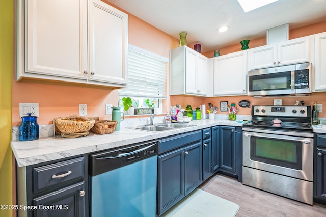 kitchen featuring light wood finished floors, stainless steel appliances, white cabinets, a sink, and blue cabinets