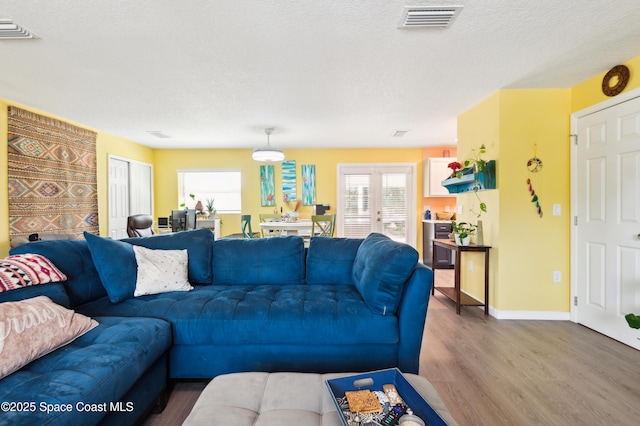 living area with french doors, visible vents, a textured ceiling, wood finished floors, and baseboards