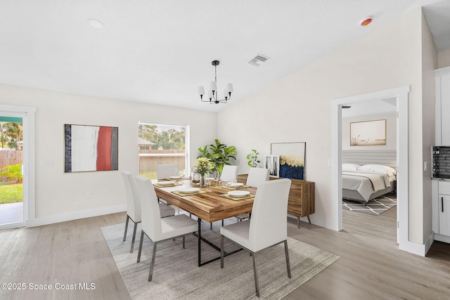 dining space with light wood finished floors, baseboards, visible vents, an inviting chandelier, and vaulted ceiling