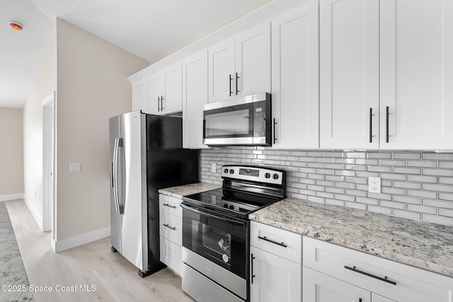 kitchen featuring tasteful backsplash, white cabinets, light wood-style flooring, light stone counters, and stainless steel appliances