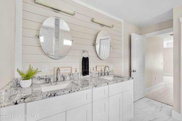 bathroom with marble finish floor, double vanity, wood walls, and a sink