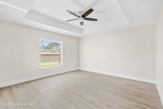 empty room with baseboards, a raised ceiling, and wood finished floors