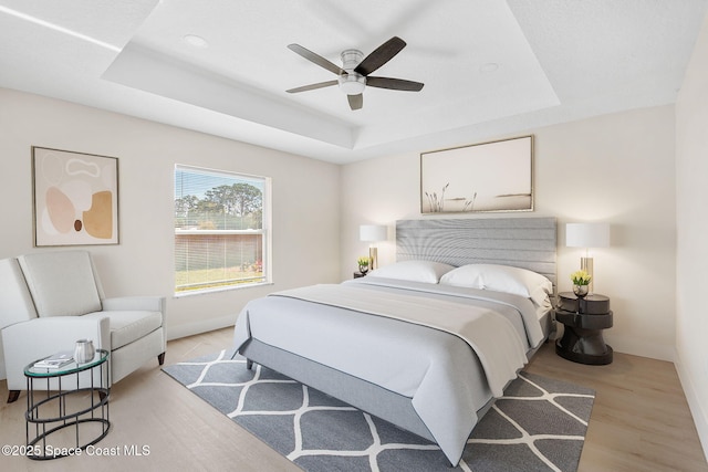 bedroom featuring light wood-type flooring, ceiling fan, and a raised ceiling