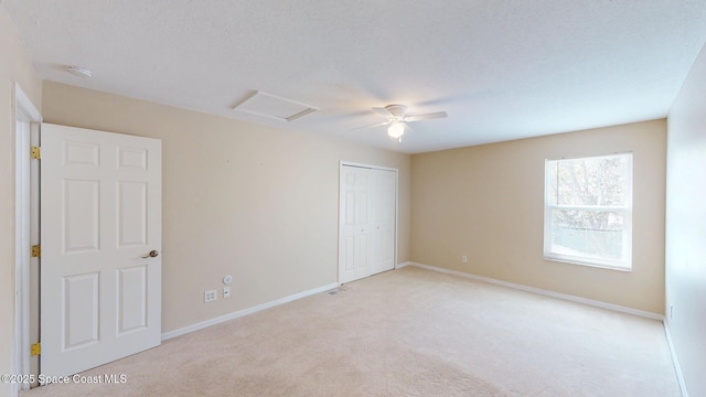 unfurnished bedroom featuring attic access, baseboards, a ceiling fan, light colored carpet, and a closet